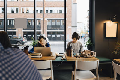 Female customers sitting at tables against window in coffee shop