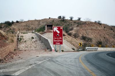 Road sign by highway against sky