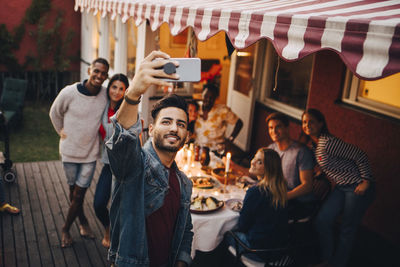 Smiling young man taking selfie with friends during dinner party