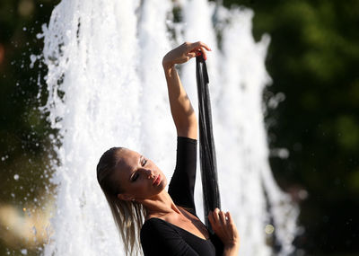 Beautiful woman with hand raised standing against fountain