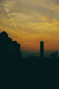 Silhouette of buildings against cloudy sky at sunset