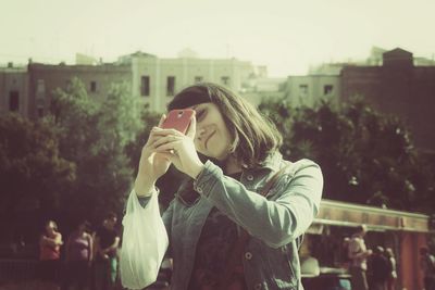 Smiling woman taking selfie while standing in city