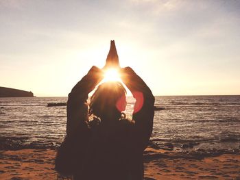 Silhouette woman hand on beach against sky during sunset