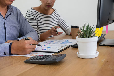 Midsection of man and woman using smart phone while sitting on table