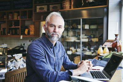 Portrait of businessman with laptop sitting at table in deli