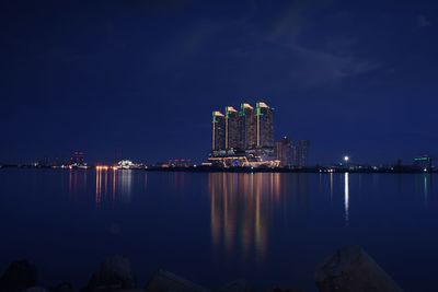 Illuminated buildings by sea against sky at night