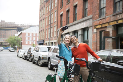 Happy mature couple taking selfie while standing with bicycles on city street