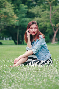 Portrait of young woman sitting on grass in field