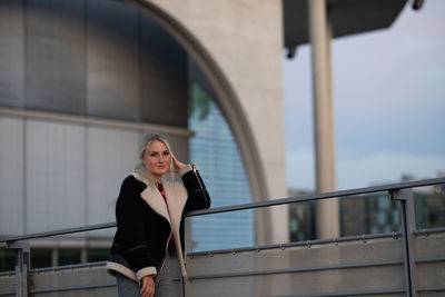Portrait of woman standing by railing against buildings