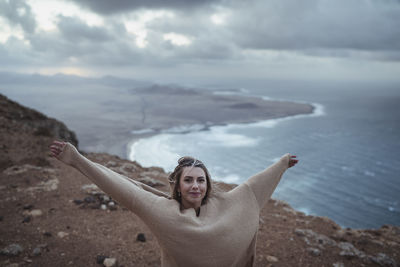 Portrait of man with arms raised in sea against sky