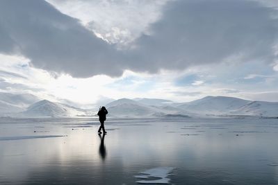 Full length of silhouette man walking on shore at beach against sky during winter