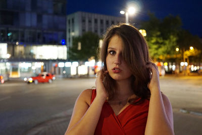 Portrait of young woman standing on illuminated street at night