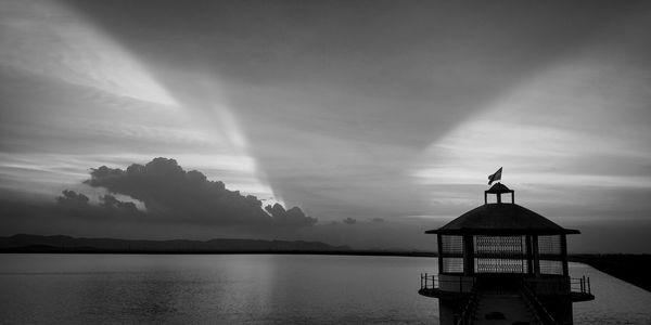 Silhouette built structure by sea against sky