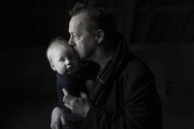 Close-up of grandfather carrying granddaughter against black background