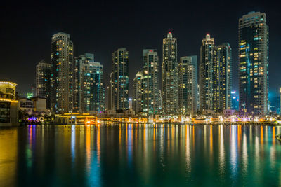 Illuminated buildings by river against sky at night