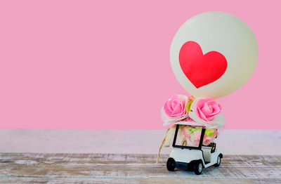 Close-up of heart shape with pink balloons against sky