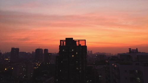 Silhouette buildings in city against orange sky