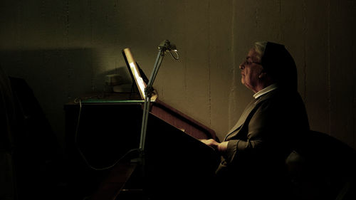 Side view of musician plying piano by wall