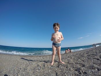 Full length of shirtless boy on beach against clear sky