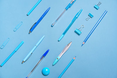 Pens pencils compasses paper clips laid out in lines all blue and background