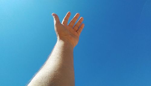 Cropped hand of man against clear blue sky during sunny day