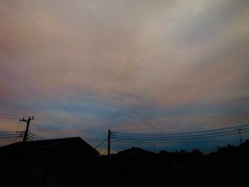 Low angle view of silhouette electricity pylons against sky at sunset