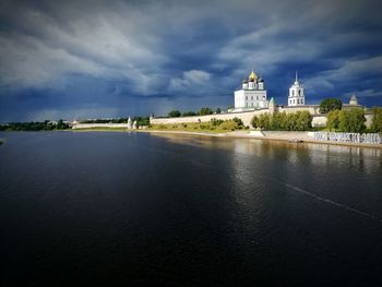 View of buildings by river against cloudy sky