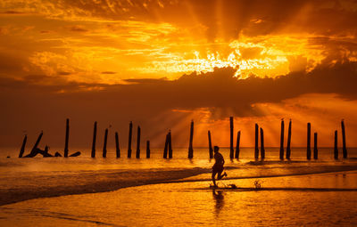 Silhouette men on wooden post by sea against sky during sunset