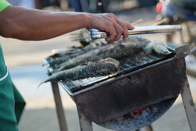 Close-up of man preparing fish on barbecue grill