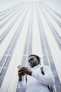 Young creative professional using smartphone against skyscraper in city