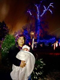 Young woman with illuminated christmas tree at night