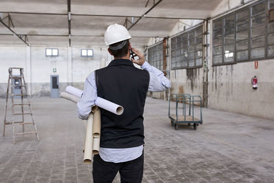 Male architect holding cardboards talking over mobile phone while standing in building