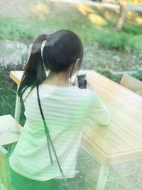 Rear view of girl using mobile phone while sitting at table