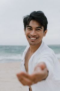 Portrait of smiling man standing at beach against sky