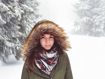 Portrait of young woman wearing warm clothing while standing in forest during winter