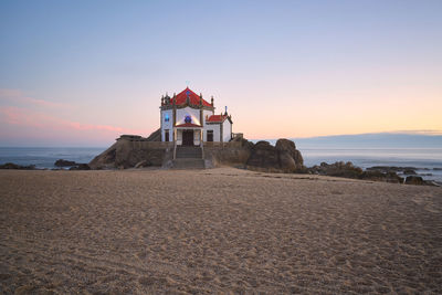 Built structure on beach by sea against sky during sunset