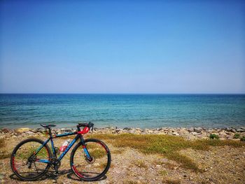 Bicycle by sea against clear blue sky