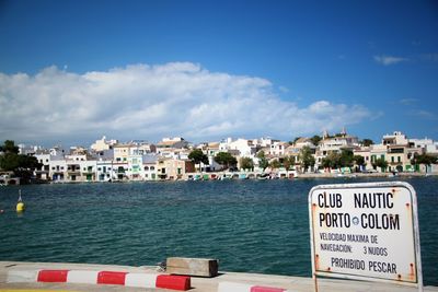 Information sign by sea against buildings in city against sky