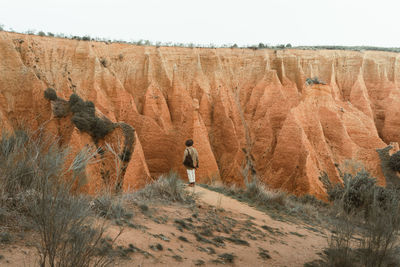 Back view of unrecognizable distant young man in casual clothes admiring arid mountain slopes during trip in highlands