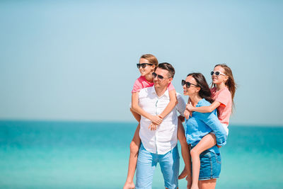 Young woman wearing sunglasses standing by sea against sky