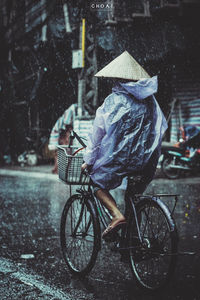 Rear view of man in raincoat riding bicycle during rainy season