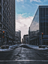 Empty city street amidst buildings against sky during winter