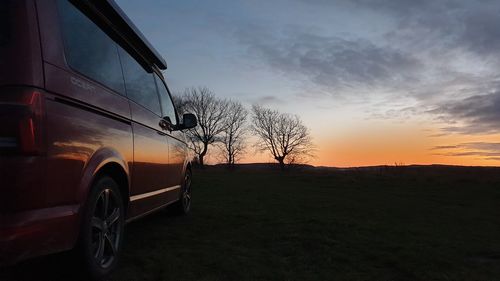 Bare tree on field against sky during sunset