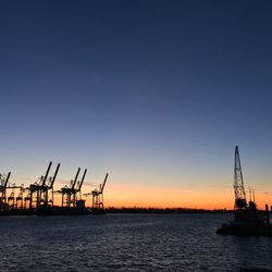 Silhouette cranes at harbor against clear sky during sunset