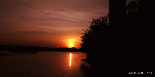 Silhouette trees by lake against sky during sunset