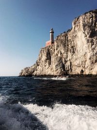 Lighthouse by sea against clear sky