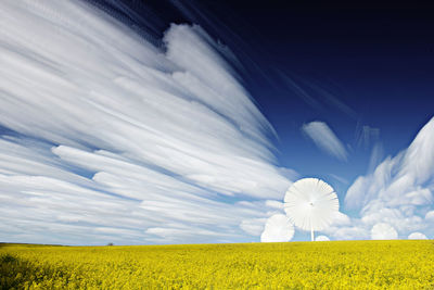 Scenic view of farm against cloudy sky during sunny day