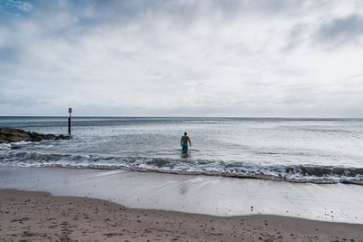 Rear view of woman walking at beach against sky