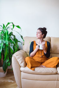 Woman having drink while sitting on sofa at home