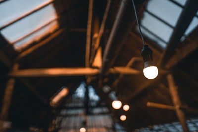 Low angle view of illuminated light bulb hanging on ceiling in building